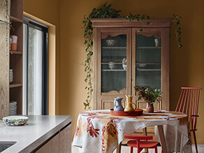 Mustard yellow dining room with marble bench tops timber cabinet and pop of orange chairs 